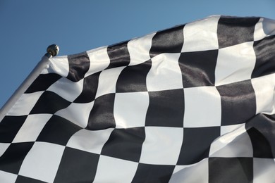 Photo of Checkered finish flag on light blue background, closeup