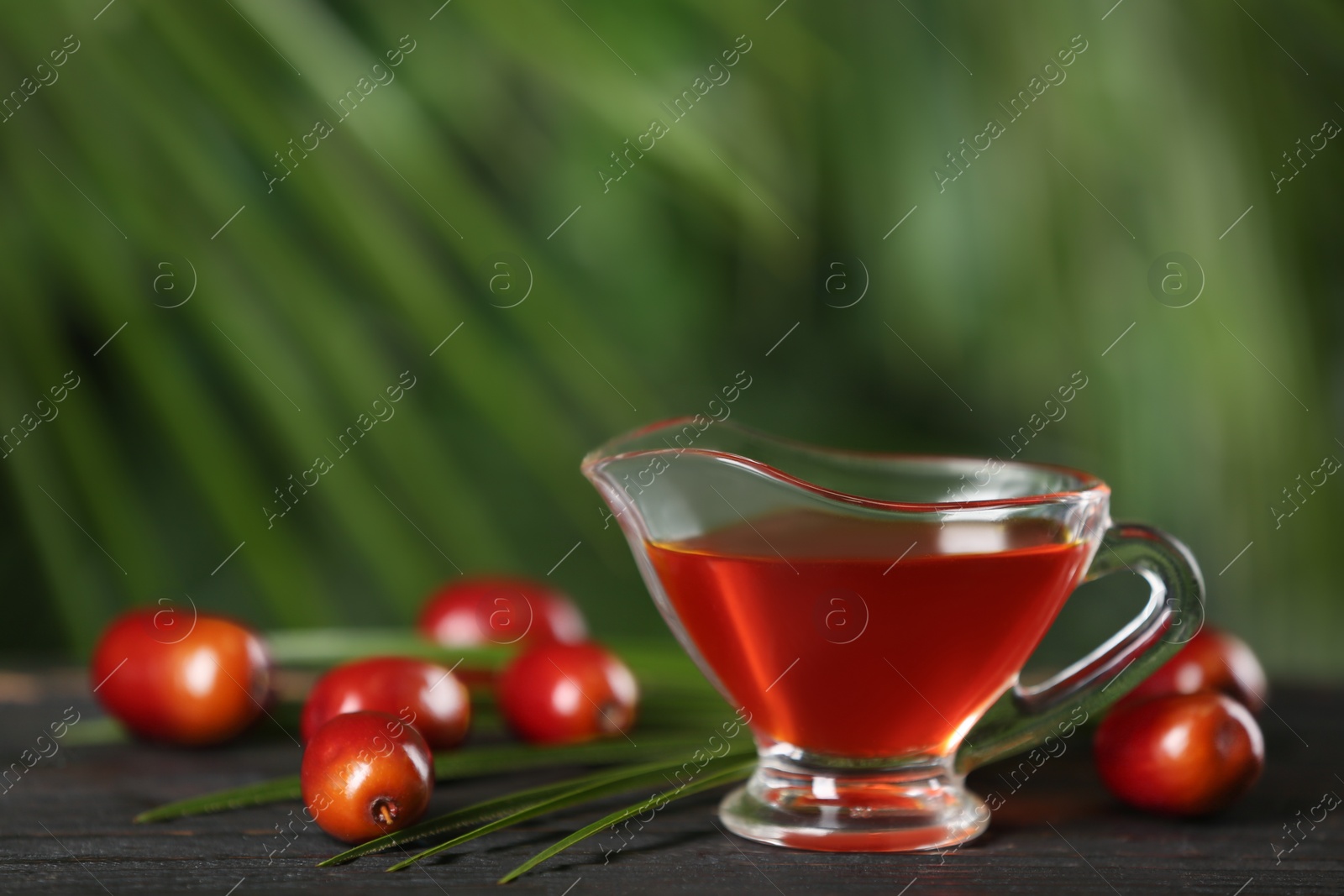 Photo of Palm oil in glass jug, tropical leaf and fruits on wooden table. Space for text