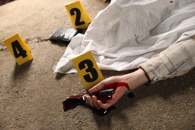 Crime scene with dead woman's body, bloody knife and markers outdoors, closeup