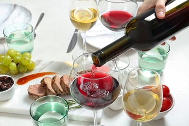 Photo of Woman pouring red wine into glass on served table