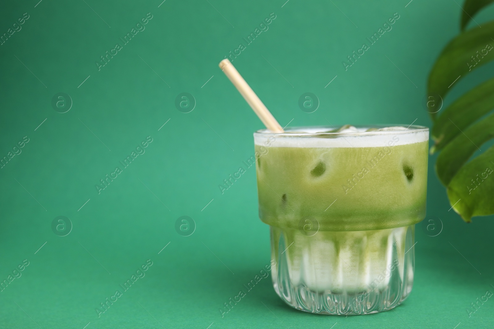 Photo of Glass of tasty iced matcha latte and leaf on green background. Space for text