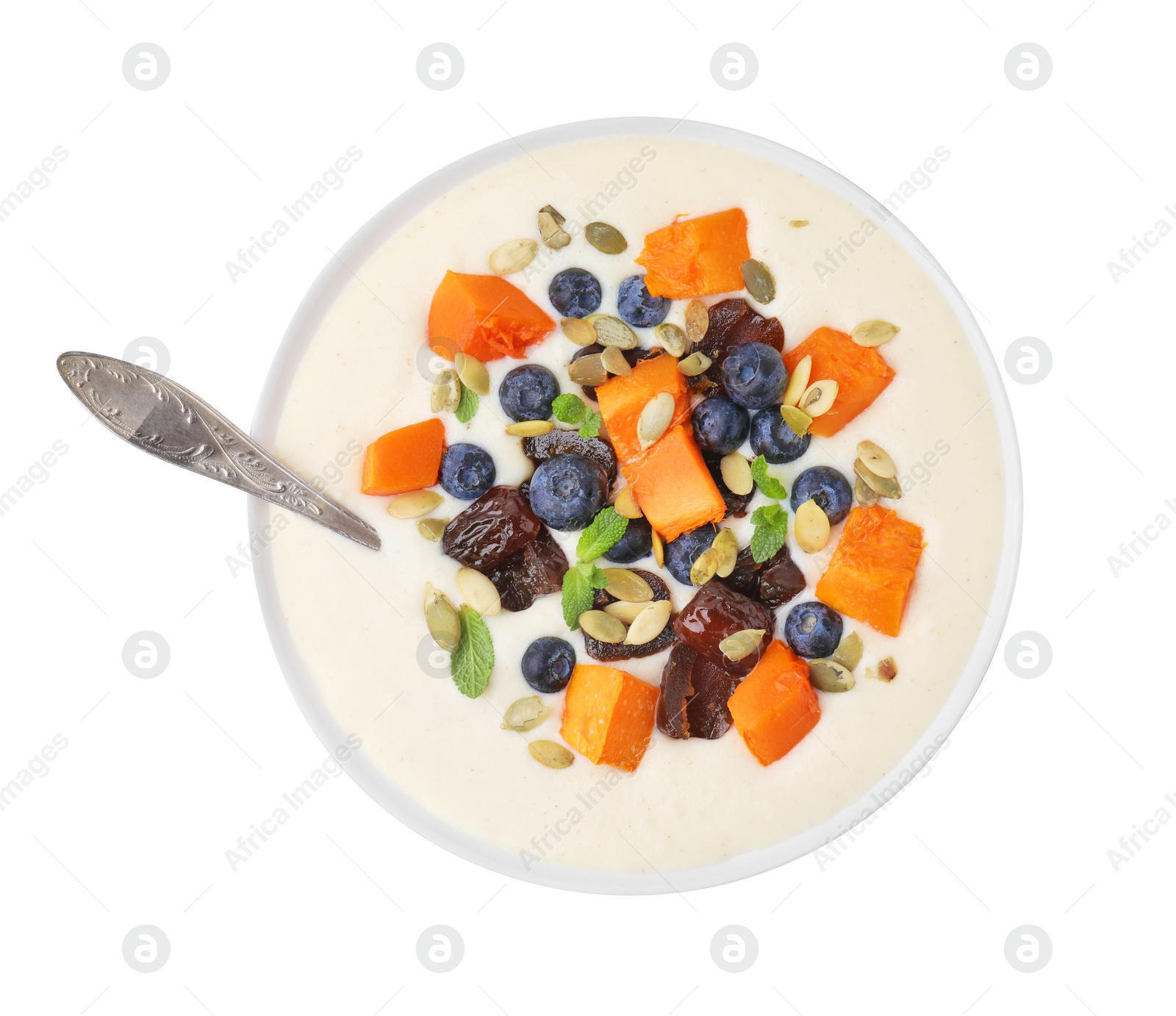 Photo of Delicious semolina pudding with blueberries, dates, pumpkin, mint and spoon in bowl isolated on white, top view