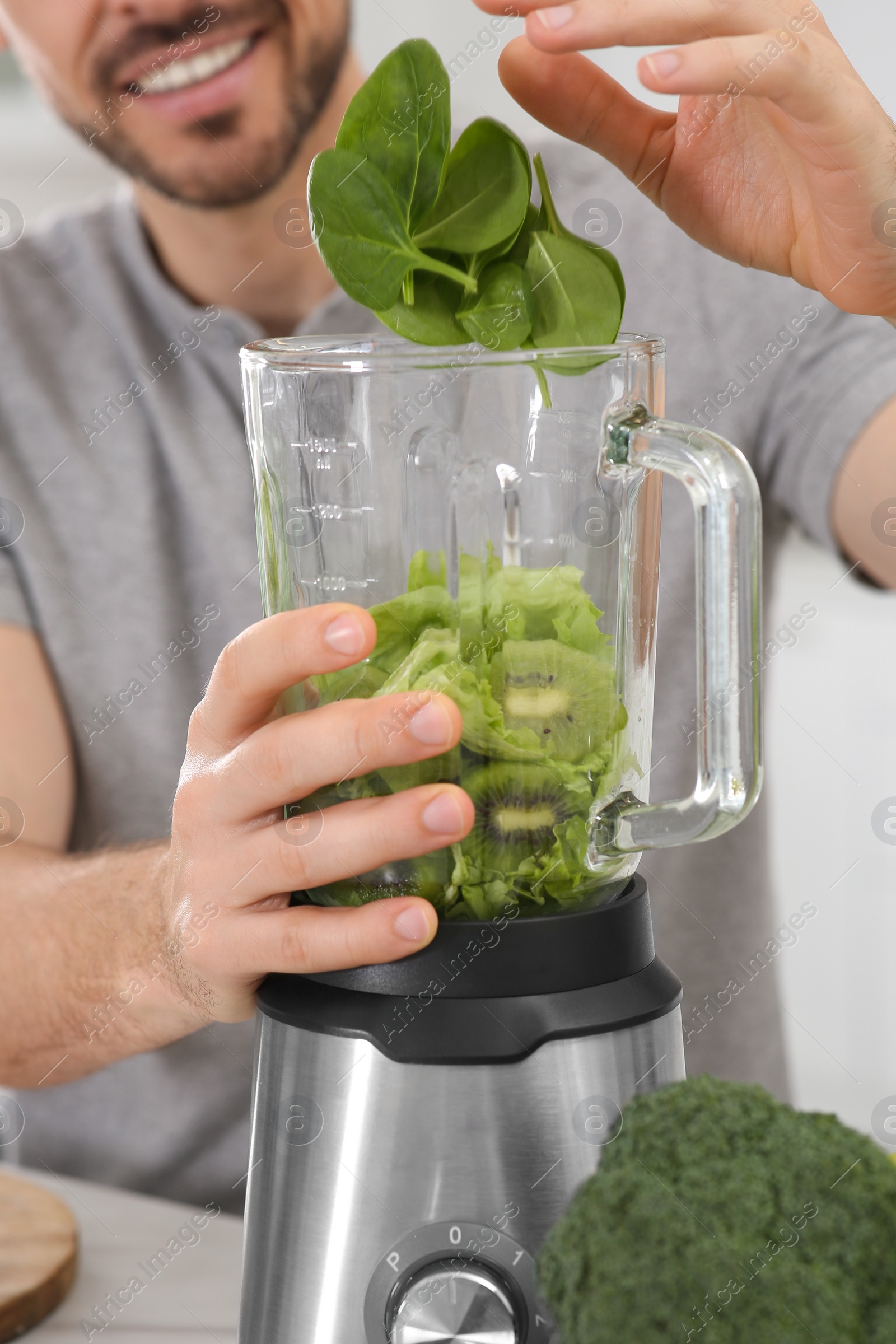 Photo of Man adding spinach leaves into blender with ingredients for smoothie at table, closeup