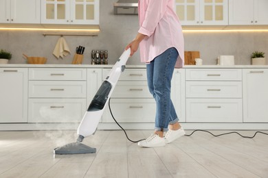 Woman cleaning floor with steam mop in kitchen at home, closeup
