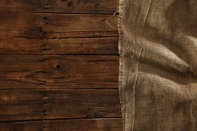 Photo of Burlap fabric on wooden table, top view. Space for text