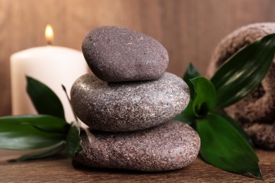Photo of Stacked spa stones, bamboo leaves, candle and towel on wooden table, closeup