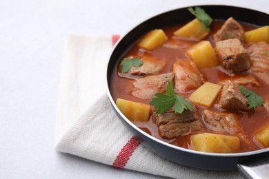 Delicious goulash in saucepan on light grey table, closeup. Space for text