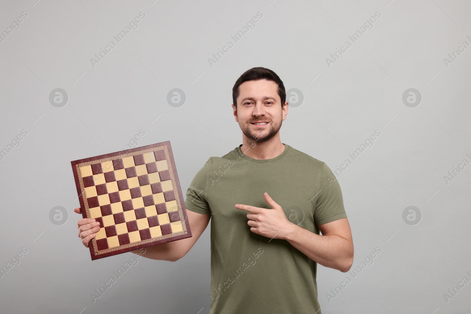 Photo of Handsome man pointing at chessboard on light grey background