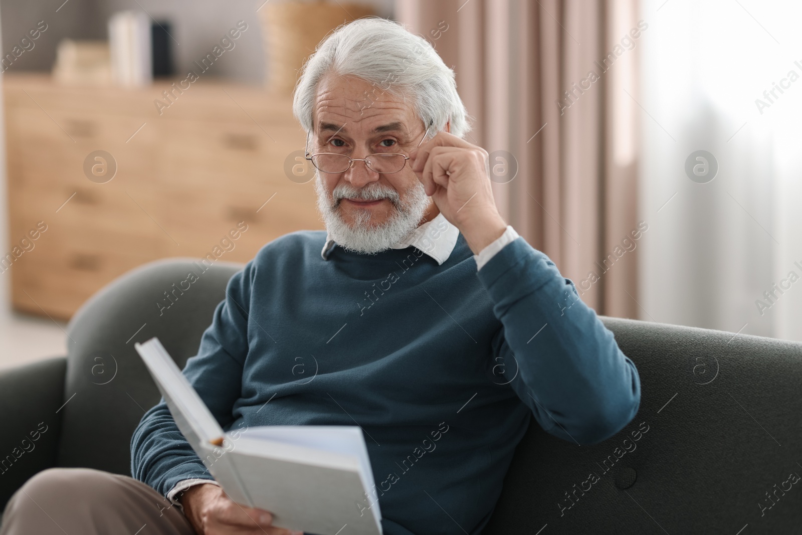 Photo of Portrait of happy grandpa reading book on sofa indoors