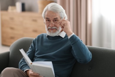 Photo of Portrait of happy grandpa reading book on sofa indoors