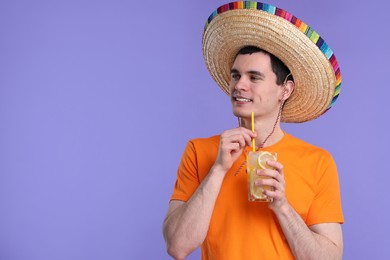 Young man in Mexican sombrero hat with cocktail on violet background. Space for text