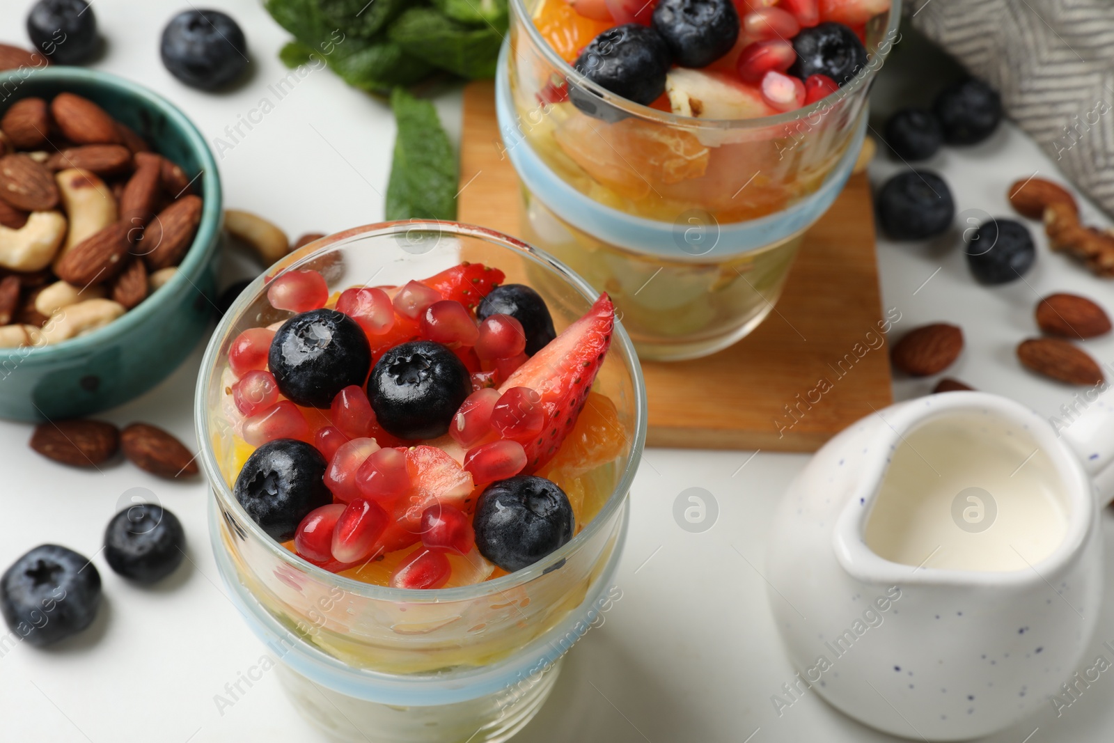 Photo of Delicious fruit salad, fresh berries, mint and nuts on white marble table