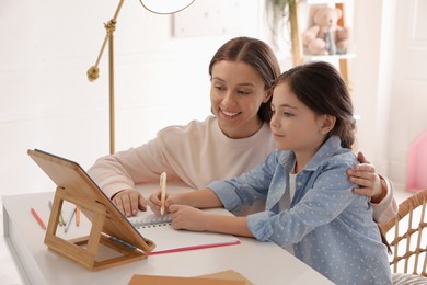 Photo of Mother helping her daughter with homework using tablet at home