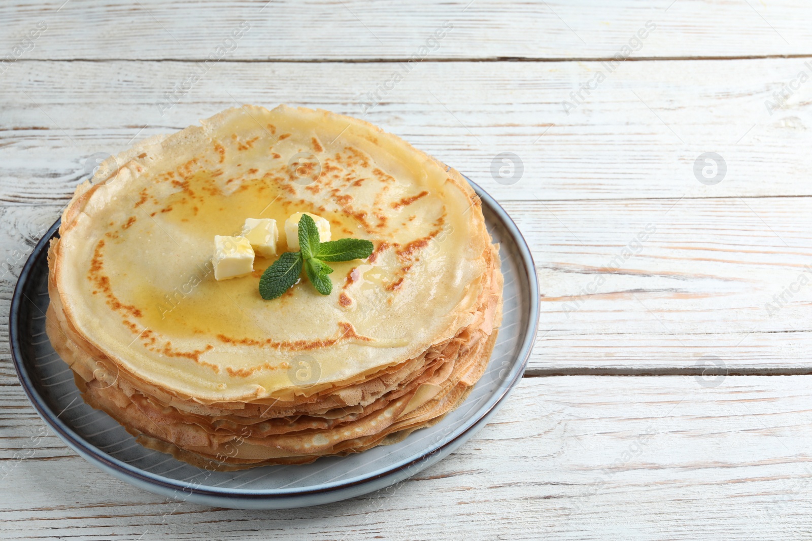 Photo of Stack of delicious crepes with mint and melting butter on white wooden table. Space for text