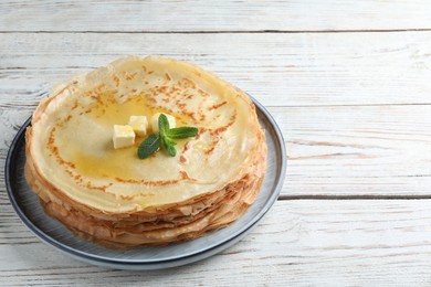 Stack of delicious crepes with mint and melting butter on white wooden table. Space for text