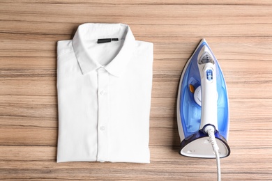 Flat lay composition with folded clean shirt and iron on wooden table