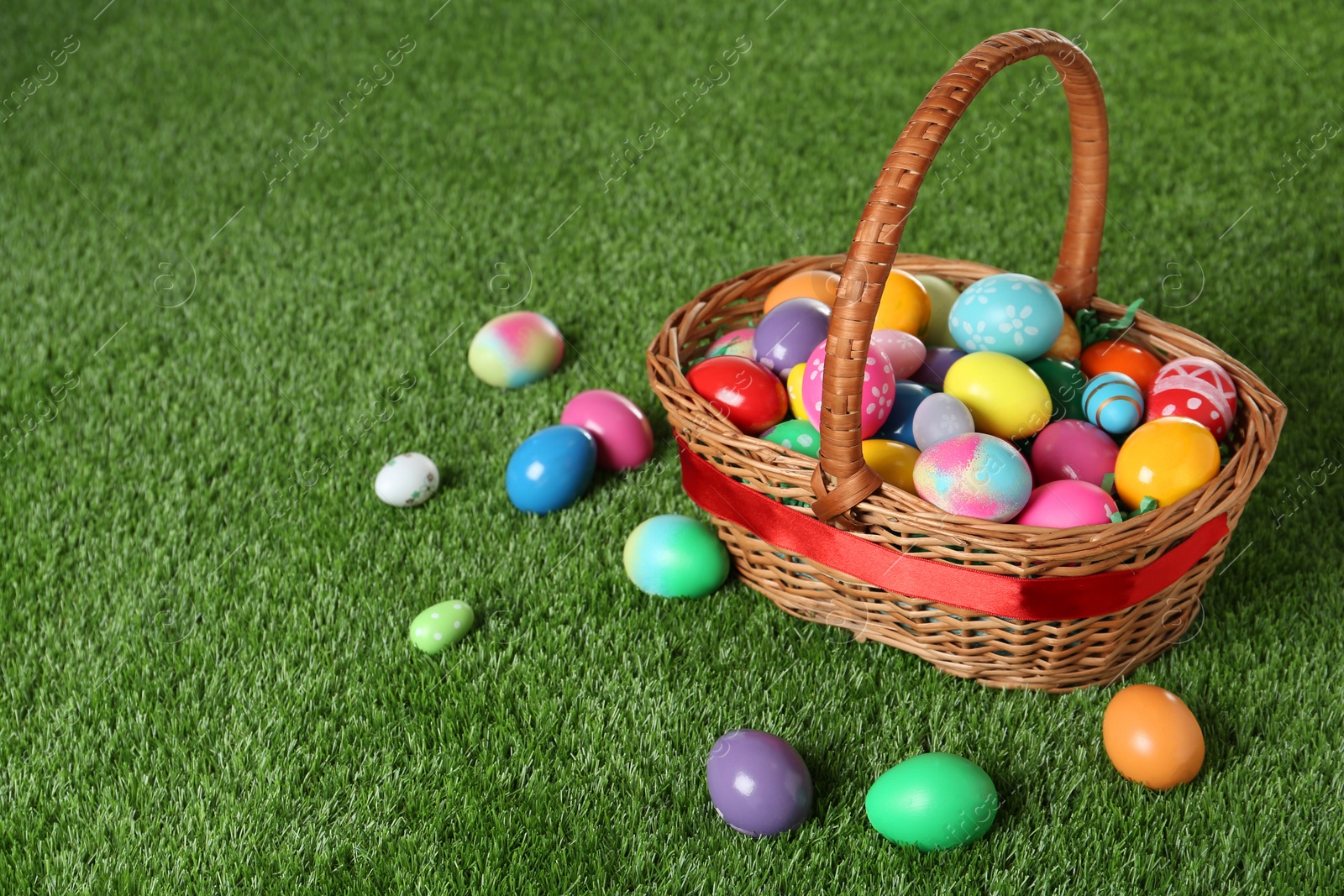 Photo of Wicker basket with Easter eggs on green grass. Space for text