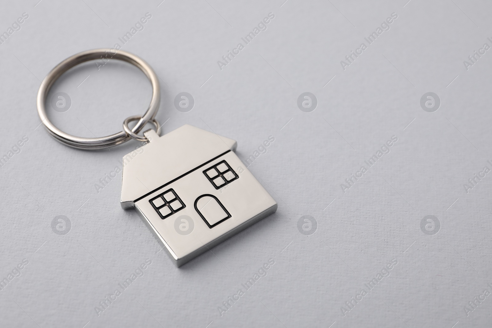 Photo of Metallic keychain in shape of house on light grey background, closeup. Space for text
