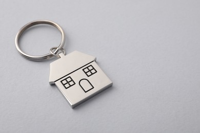 Metallic keychain in shape of house on light grey background, closeup. Space for text