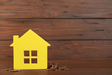 Photo of House model and coins on wooden background. Space for text