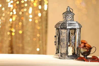 Arabic lantern, misbaha and dates on table against blurred lights, space for text