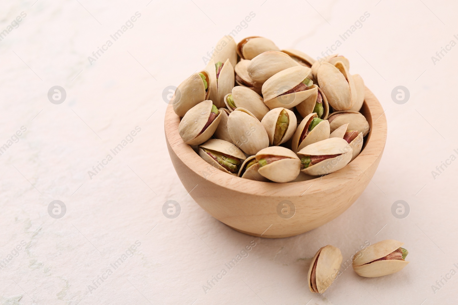 Photo of Delicious pistachios in bowl on white textured table. Space for text