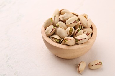 Photo of Delicious pistachios in bowl on white textured table. Space for text