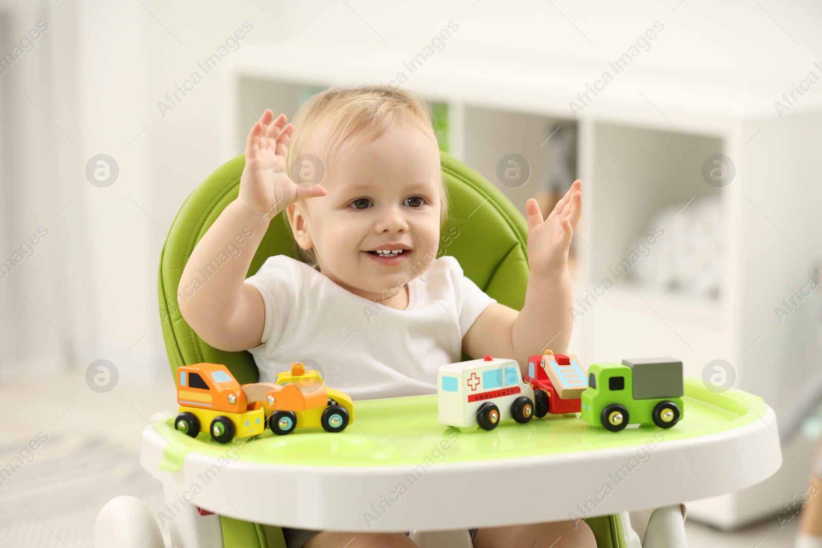 Photo of Children toys. Cute little boy playing with toy cars in high chair at home