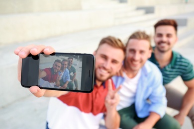 Photo of Happy young men taking selfie outdoors, focus on smartphone