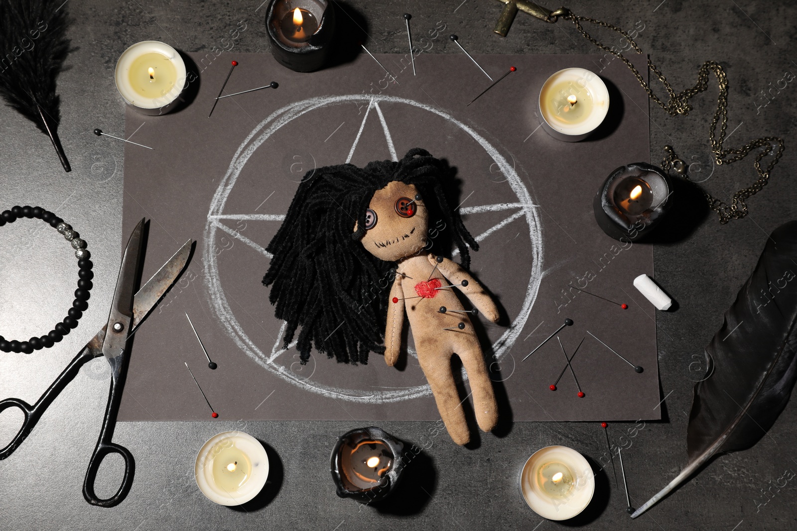 Photo of Female voodoo doll pierced with pins and ceremonial items on grey table, flat lay