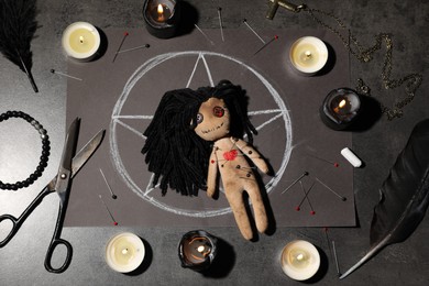 Photo of Female voodoo doll pierced with pins and ceremonial items on grey table, flat lay