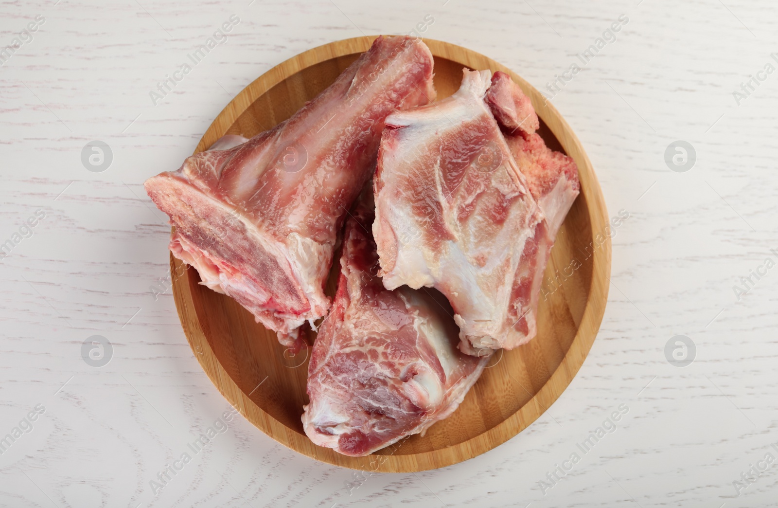 Photo of Plate with raw chopped meaty bones on white wooden table, top view