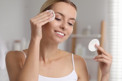Photo of Smiling woman removing makeup with cotton pads in bathroom