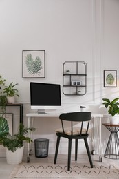 Comfortable workplace with modern computer and houseplants in room. Interior design