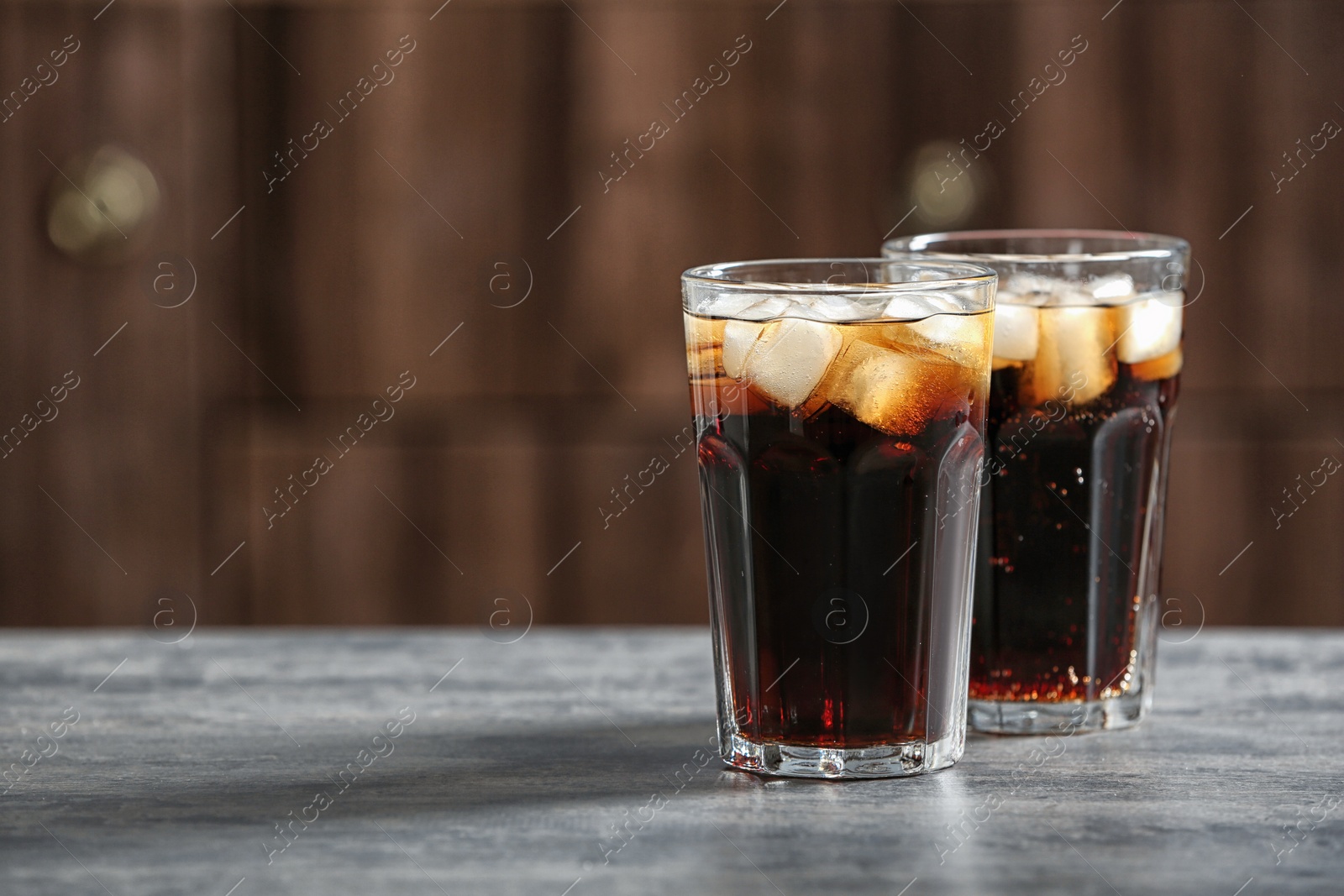 Photo of Glasses of cold cola on table against blurred background. Space for text