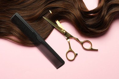 Photo of Professional hairdresser scissors and comb with brown hair strand on pink background, top view