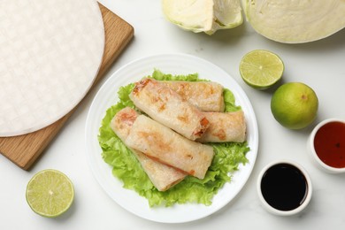 Photo of Delicious fried spring rolls served on white marble table, flat lay