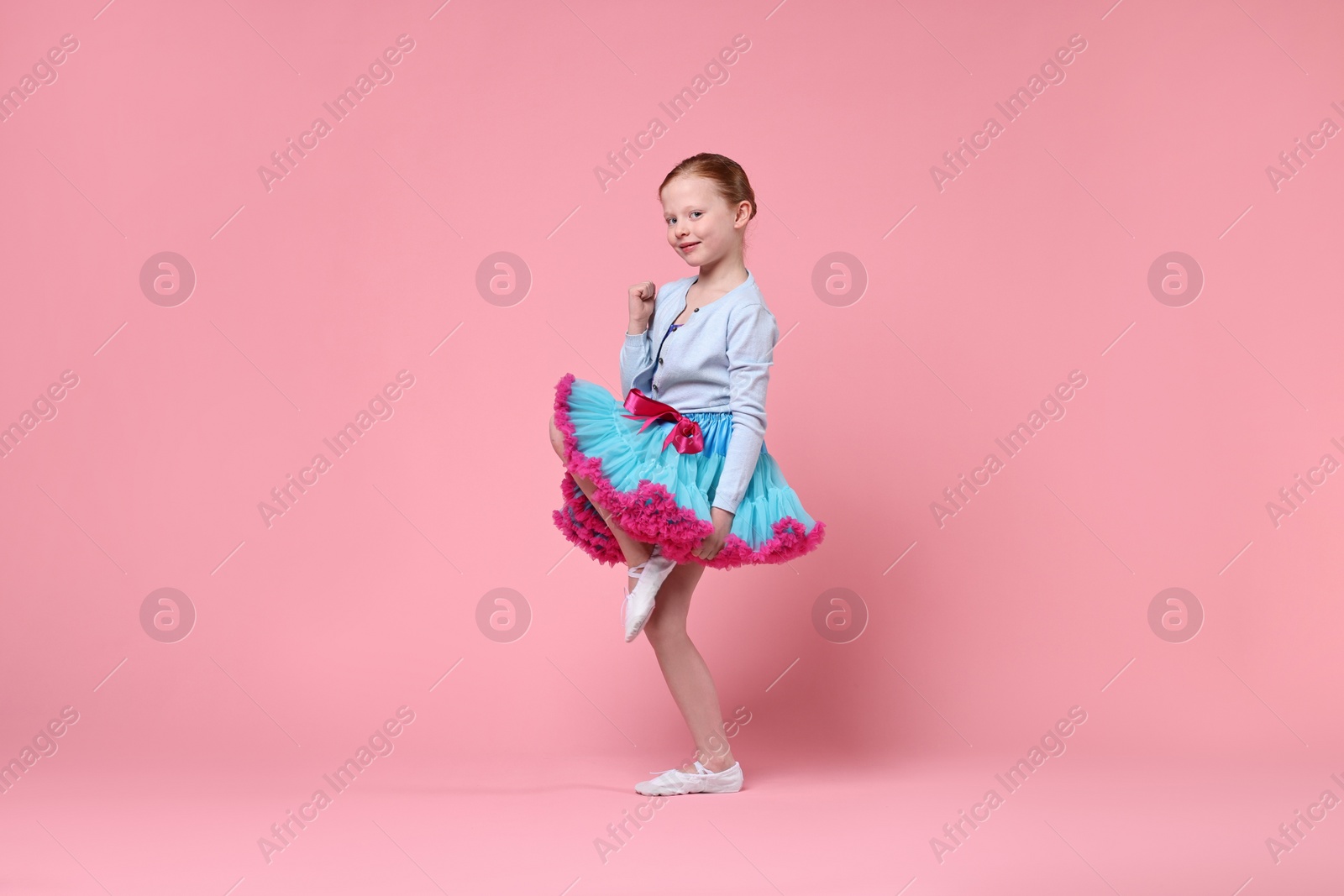 Photo of Cute little girl dancing on pink background