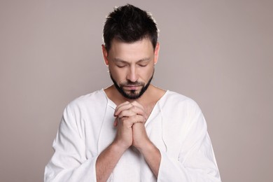 Religious man with clasped hands praying against grey background