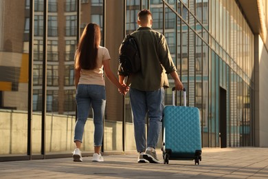 Photo of Long-distance relationship. Young couple with luggage walking near building outdoors, back view