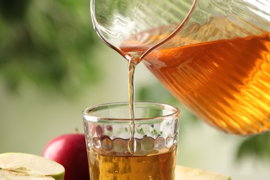 Pouring apple juice into glass on blurred green background, closeup