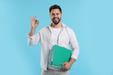 Happy man with folder showing OK gesture on light blue background