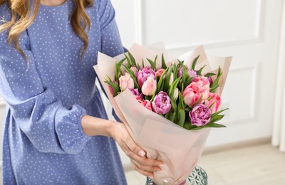 Photo of Woman putting bouquet of beautiful tulips in vase indoors, closeup