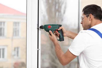 Construction worker repairing plastic window with electric screwdriver indoors