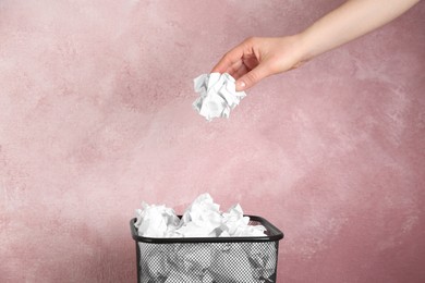 Photo of Woman throwing crumpled paper ball into basket on pink background, closeup