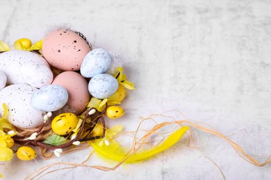 Photo of Decorative nest with many painted Easter eggs on light textured background, closeup. Space for text