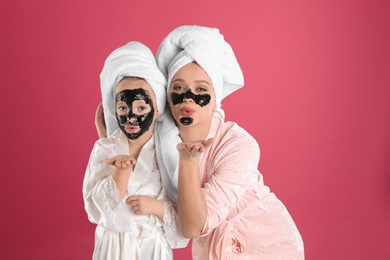 Happy mother and daughter with black facial masks on pink background