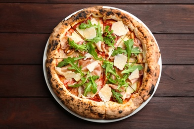 Photo of Tasty pizza with meat and arugula on wooden table, top view