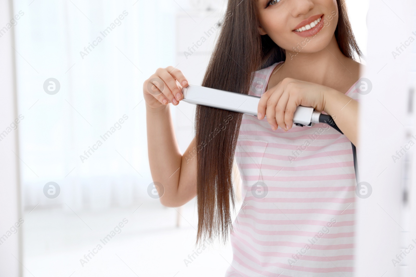 Photo of Happy woman using hair iron in front of mirror, closeup. Space for text