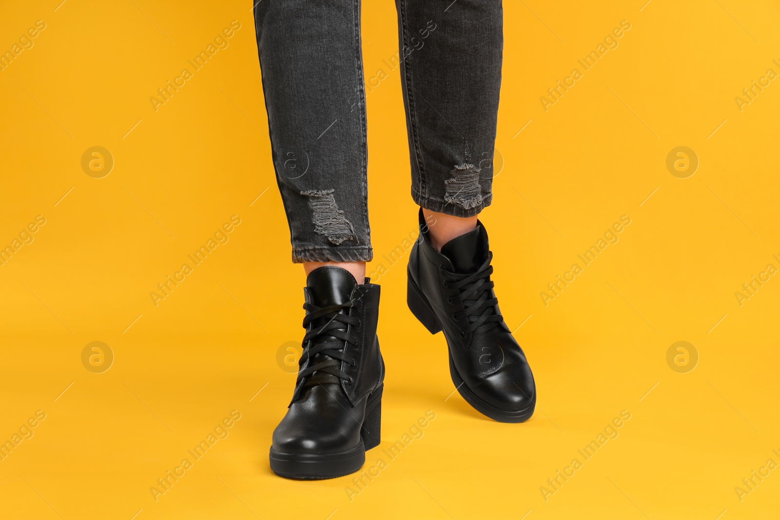 Photo of Woman wearing stylish boots on yellow background, closeup